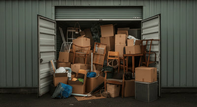 Outside view of a cluttered storage unit with cardboard boxes, furniture, and items overflowing from the open door.