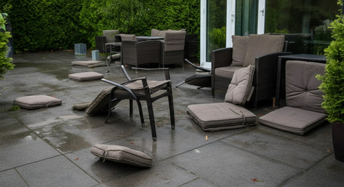 Patio with overturned chairs and scattered cushions after a windy day.
