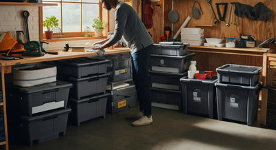 Person cleaning and organizing plastic storage bins in a home or garage setting.
