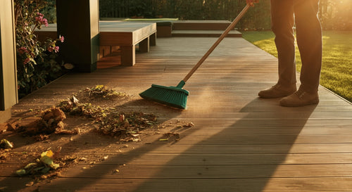 Person sweeping leaves and debris off a wooden patio or deck area.