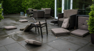 Patio with overturned chairs and scattered cushions after a windy day.