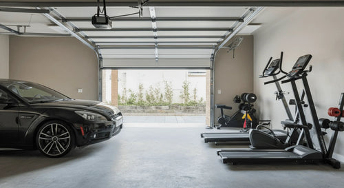 Garage with a parked car and exercise equipment set up side by side in a tight space.