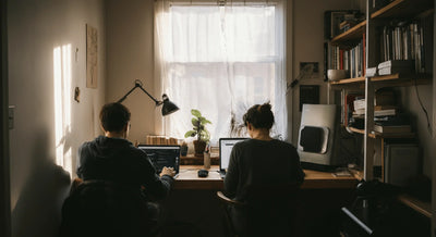 Cramped home office with two people working on laptops at a shared desk.